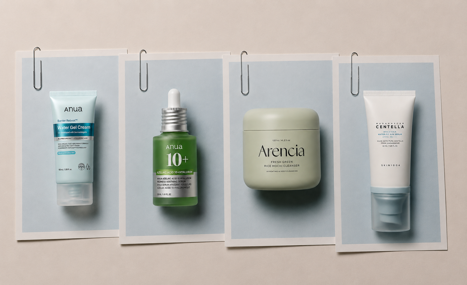 Four skincare products displayed on light blue paper sheets with silver paper clips, arranged horizontally with slight tilts and overlapping layers against a soft beige background.