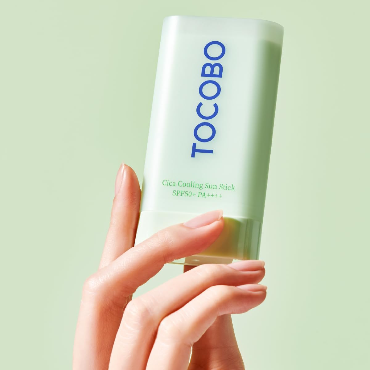 Hand holding a Tocobo Cica Cooling Sun Stick against a light green background