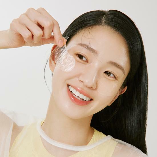 Woman applying a Goodal VITA-C Dark Spot Care Eye Patch with a white background