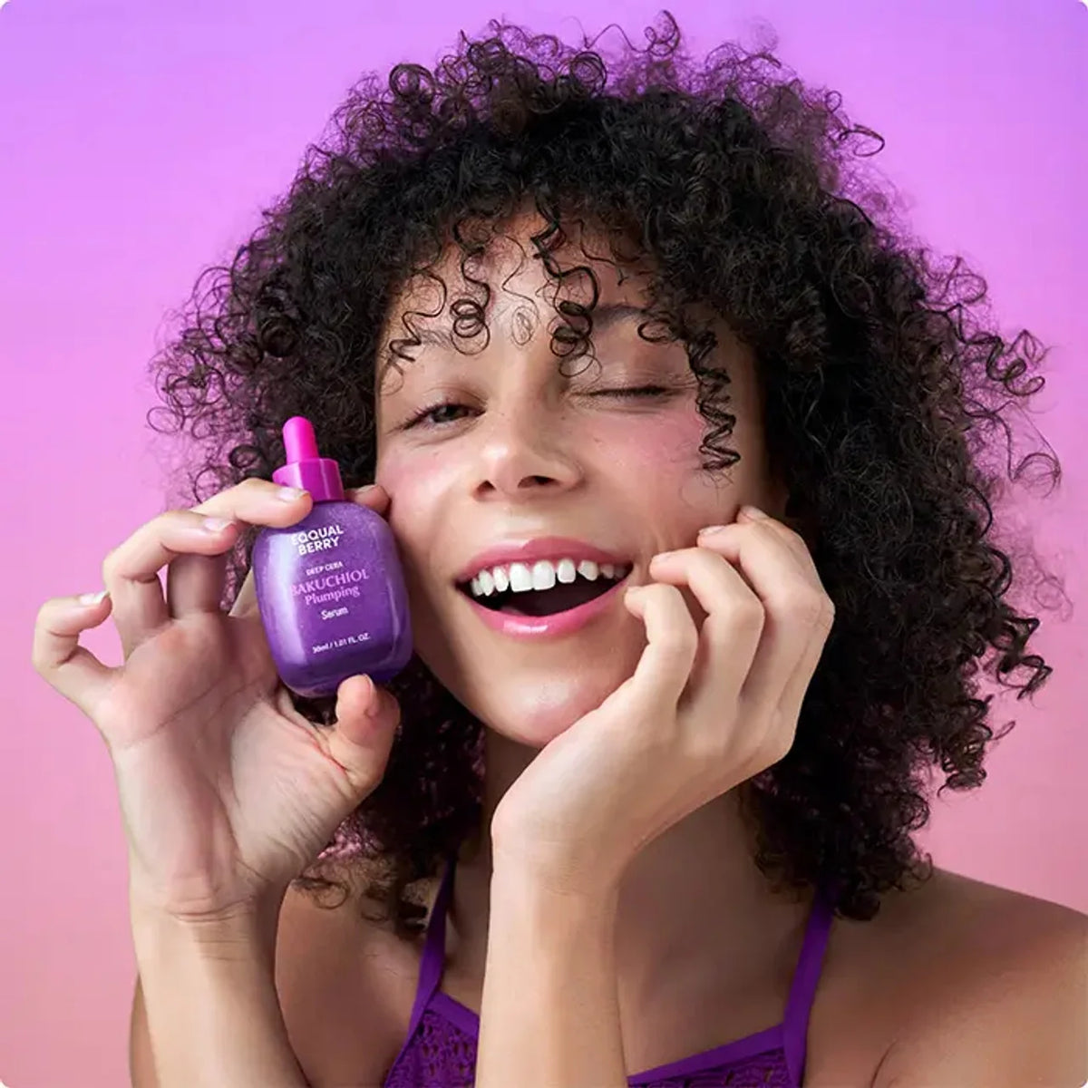 Woman holding a EQQUALBERRY Bakuchiol Plumping Serum 30 ml bottle of hair product against a pink background