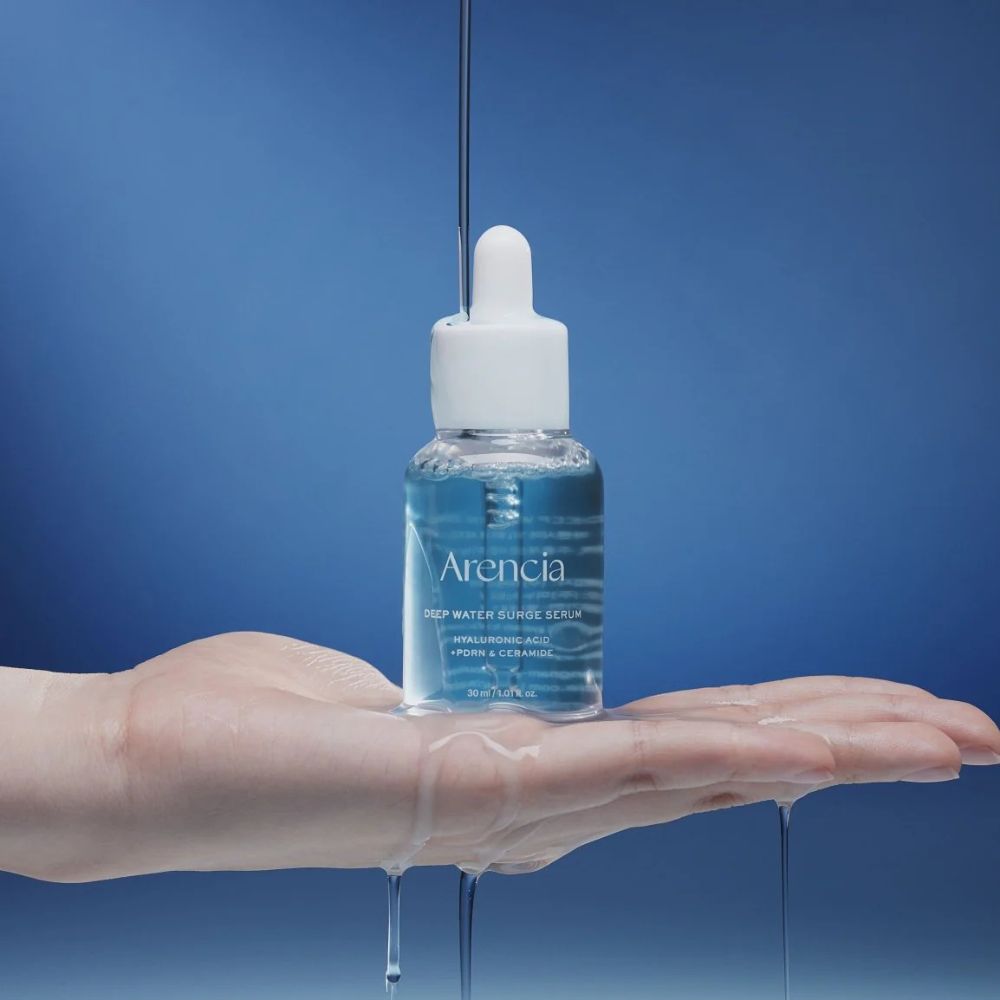 Bottle of Arencia Deep Water Surge Serum being held over a hand with a blue background