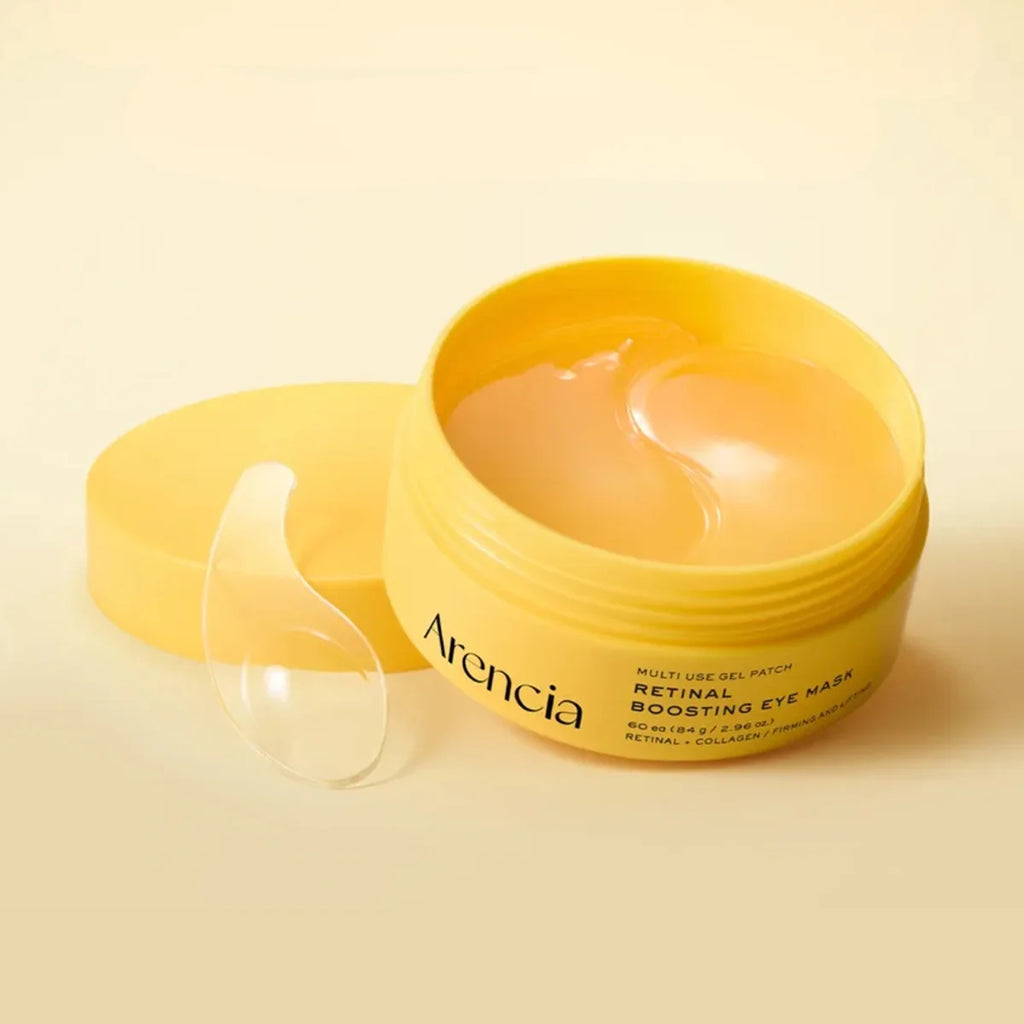 An open yellow jar of Arencia Retinal Boosting Eye Mask with a clear gel patch visible inside, alongside its matching yellow lid on a warm cream background.