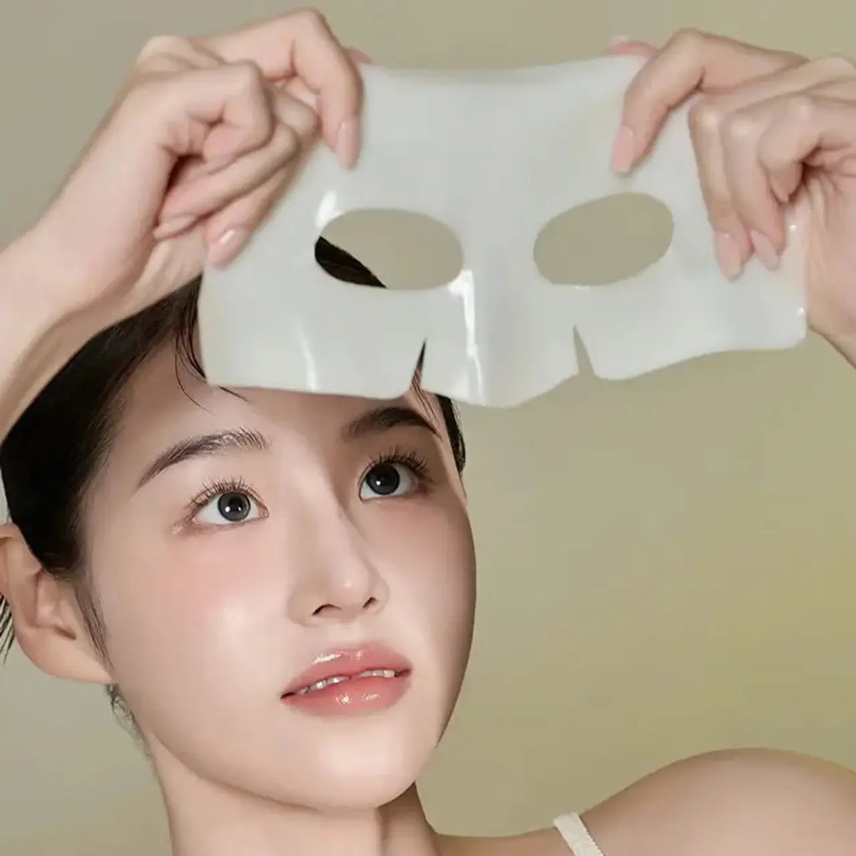 Woman holding a Biodance Radiant Vita Niacinamide Real Deep Mask over her face against a plain background