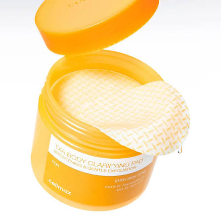 An open yellow jar of Cellmax TXA Body Clarifying Pad with a textured cream pad partially pulled out, on a white background.