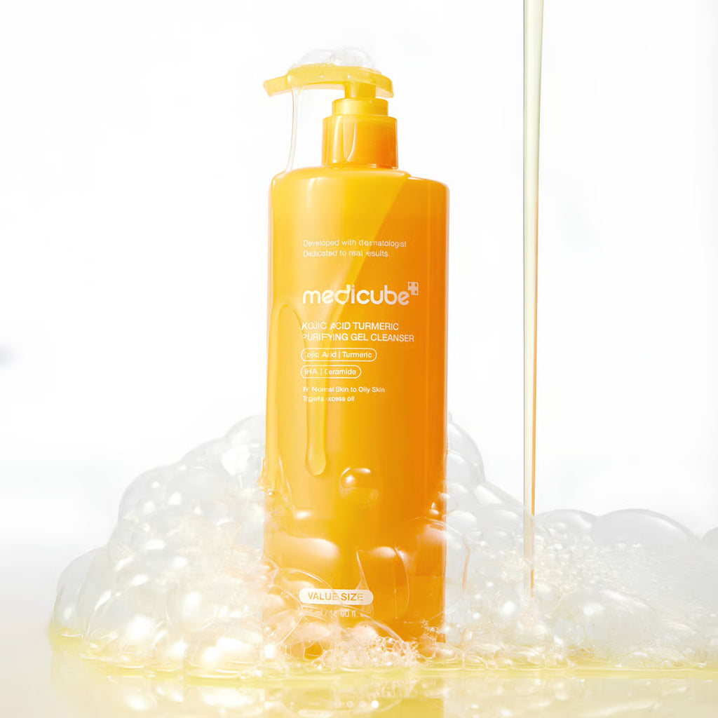 A bottle of medicube Acid Turmeric Cleansing Gel stands on a reflective white surface surrounded by foam, with a stream of yellow gel running vertically on the right side.