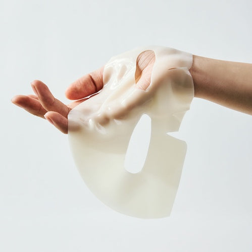 A translucent, flexible silicone Biodance Radiant Vita Niacinamide Real Deep Mask being worn on a person's hand and wrist, shown against a clean light gray background.