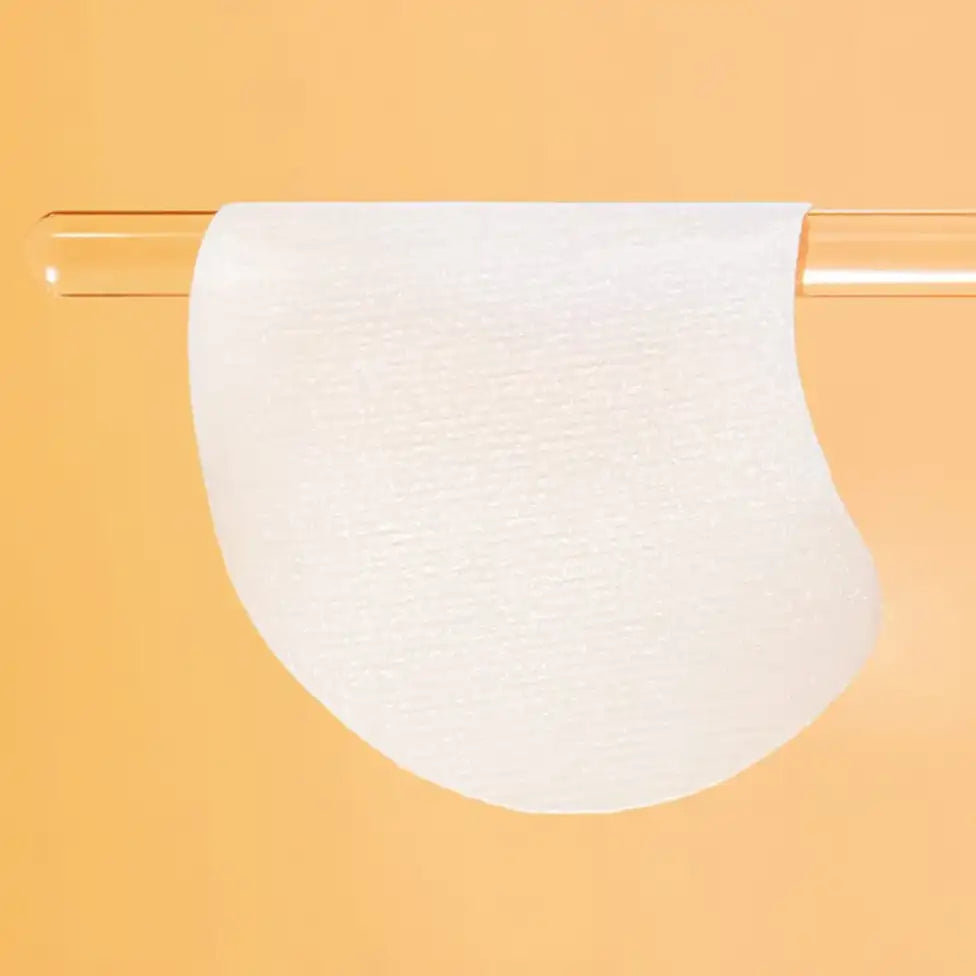 Celimax Pore + Dark Spot Brightening Face Pads with a curved bottom edge, draped over a clear cylindrical rod against a solid warm orange background.