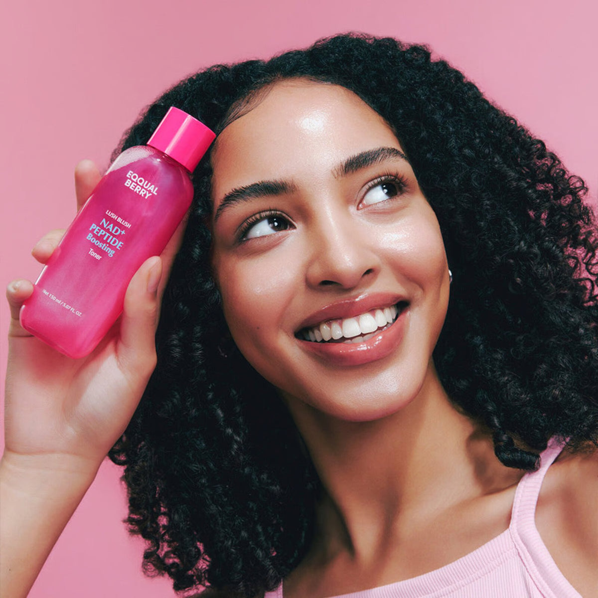 Woman holding a EQQUALBERRY Nad+ Peptide Boosting Toner 150 ml against a pink background