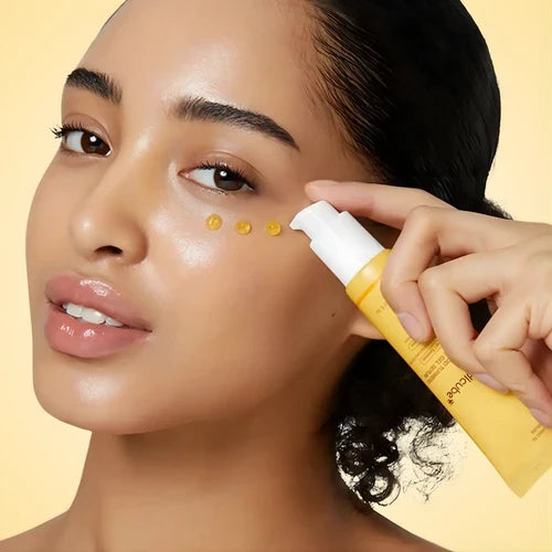 Person applying medicube eye cream kojic acid to their face with a yellow bottle on a beige background