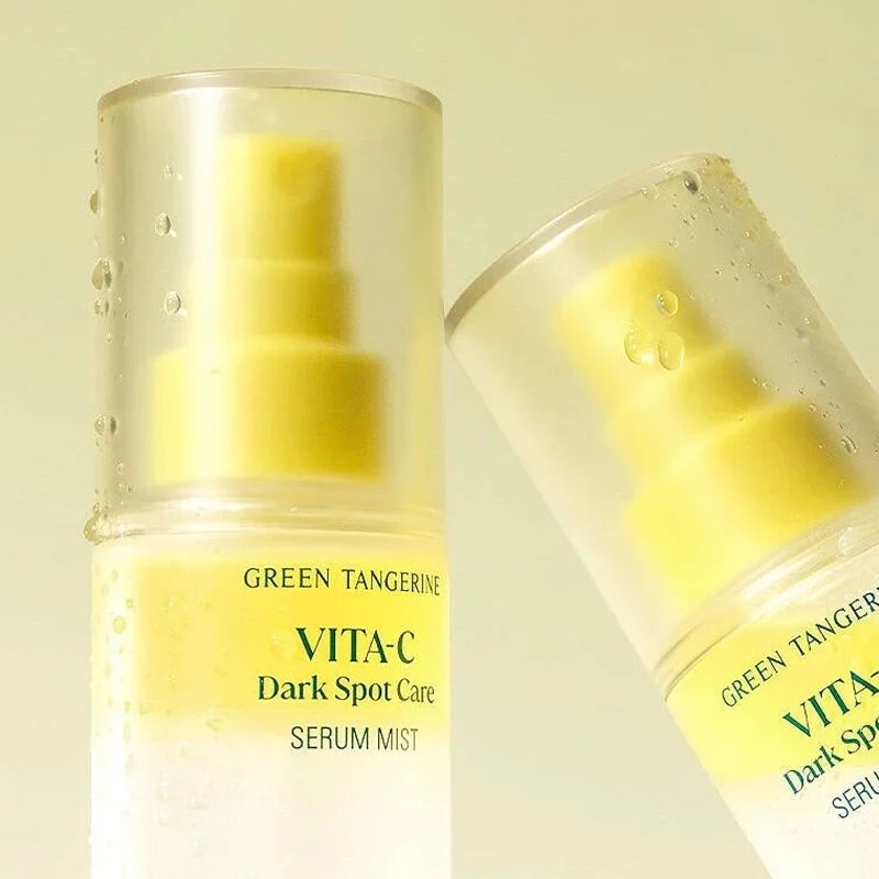 Two bottles of goodal VITA-C Dark Spot Care Serum Mist, one upright and one tilted, showing a translucent clear cap, yellow pump, and white bottle with green text on a pale yellow background.