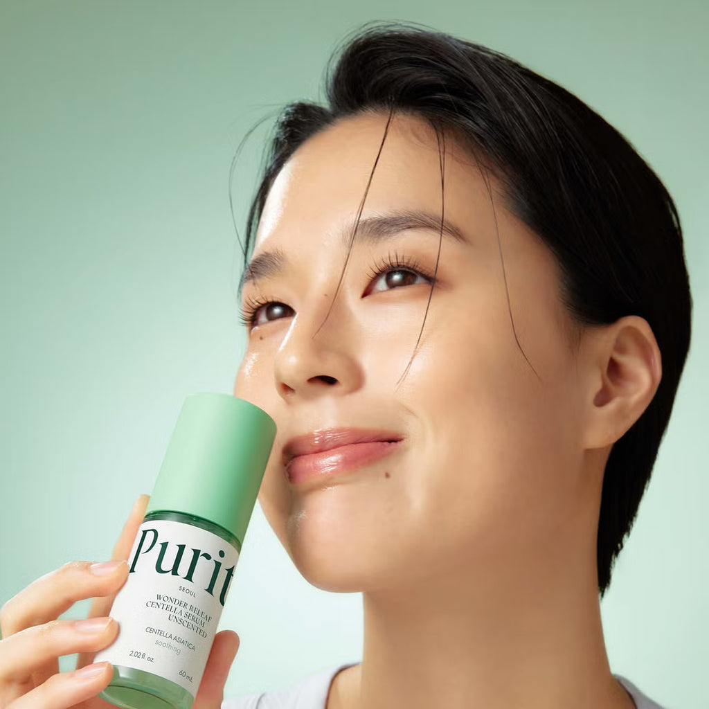 A woman with short dark hair holds a green bottle of Purito Wonder Releaf Centella Unscented Serum against a soft mint green background.
