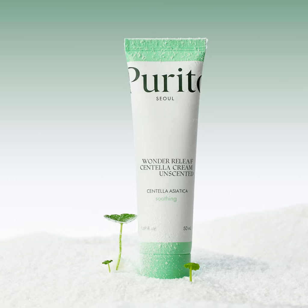 A tube of Purito Wonder Releaf Centella Unscented Cream, unscented, standing upright in white sand with small green plant sprouts. The background is a soft, light green gradient.