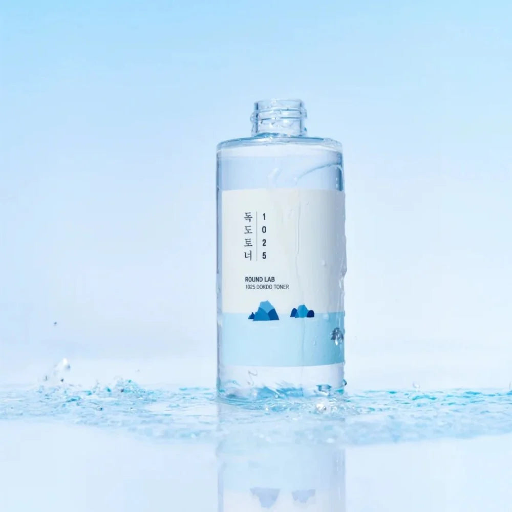 Round Lab 1025 Dokdo Toner  and blue graphic accents, standing in splashing water against a light blue gradient background.