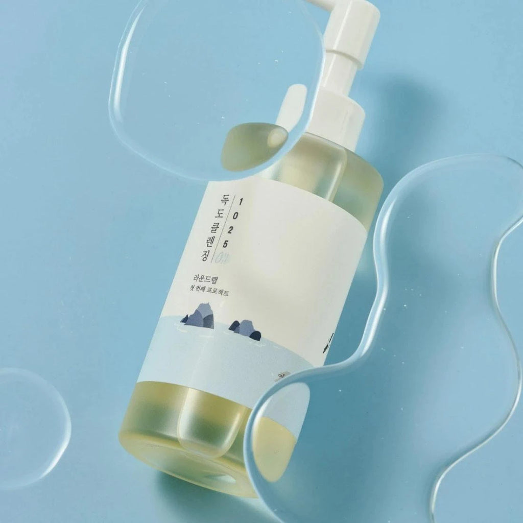 Round Lab 1025 Dokdo Cleansing OilRound Lab 1025 Dokdo Cleansing Oil, photographed on a light blue background with translucent wavy props.