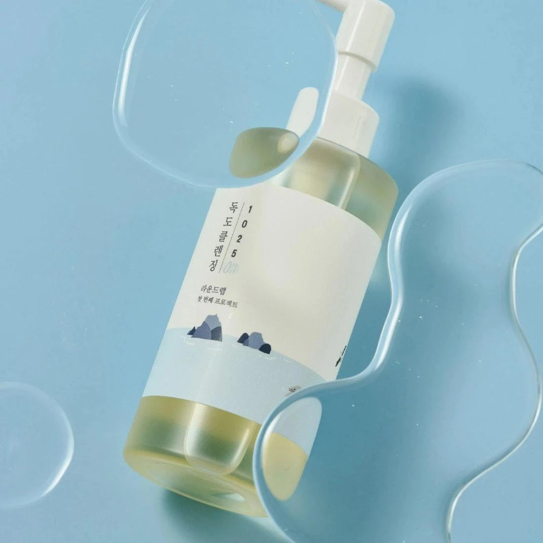 Round Lab 1025 Dokdo Cleansing OilRound Lab 1025 Dokdo Cleansing Oil, photographed on a light blue background with translucent wavy props.