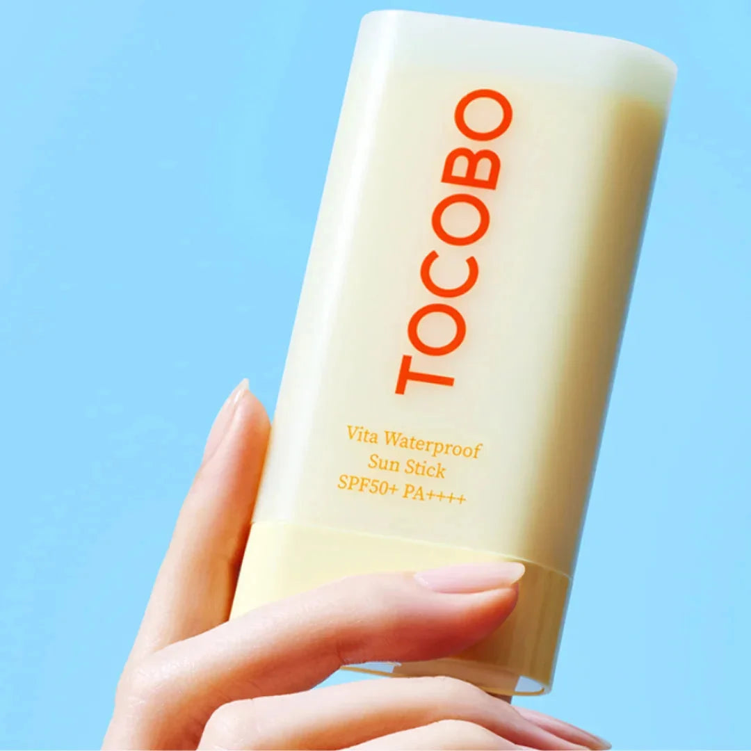 A hand holding a Tocobo Vita Waterproof Sun Stick  against a solid light blue background.